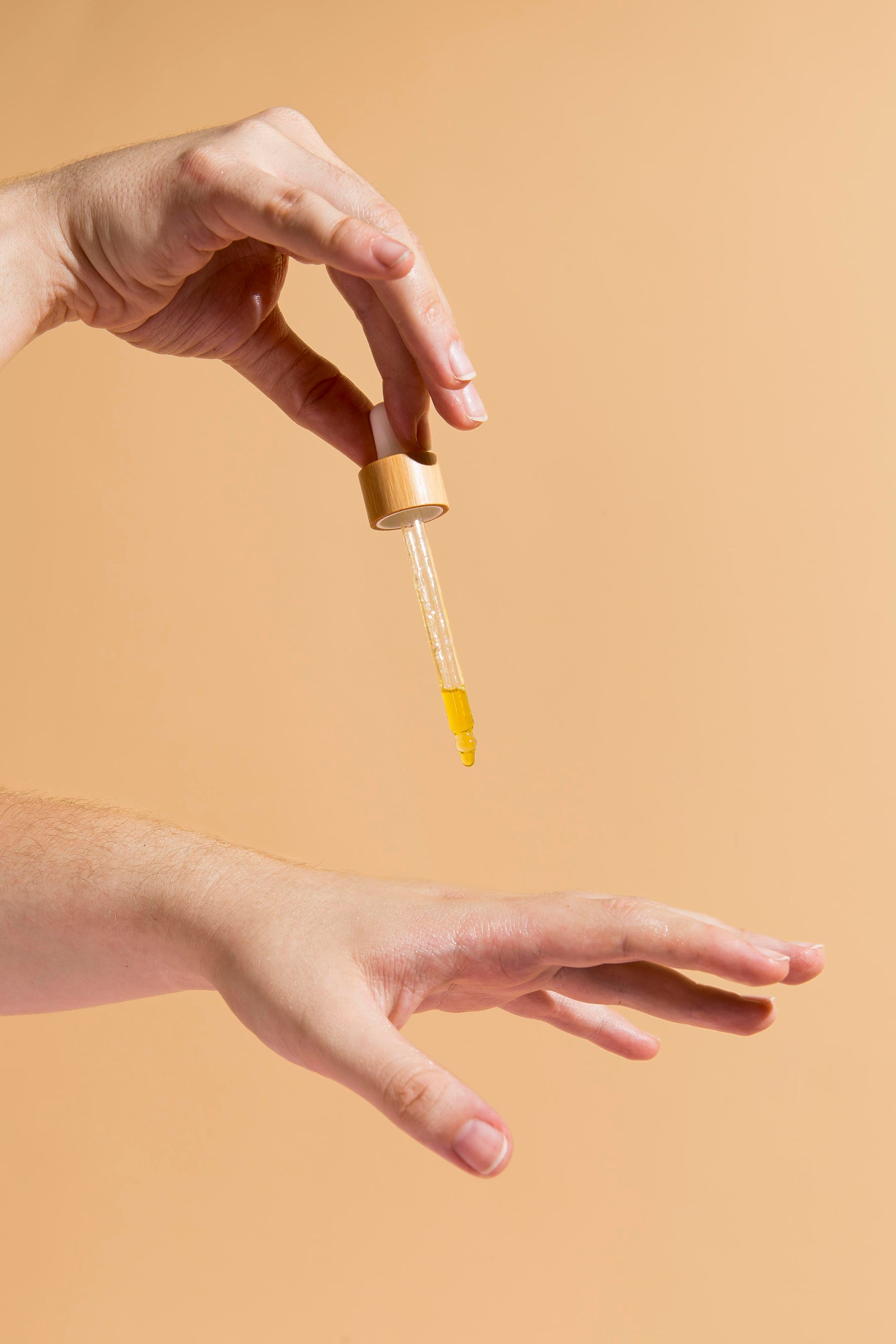 Pipette mit goldenem Öl tropft auf Unterarm vor beigem Hintergrund