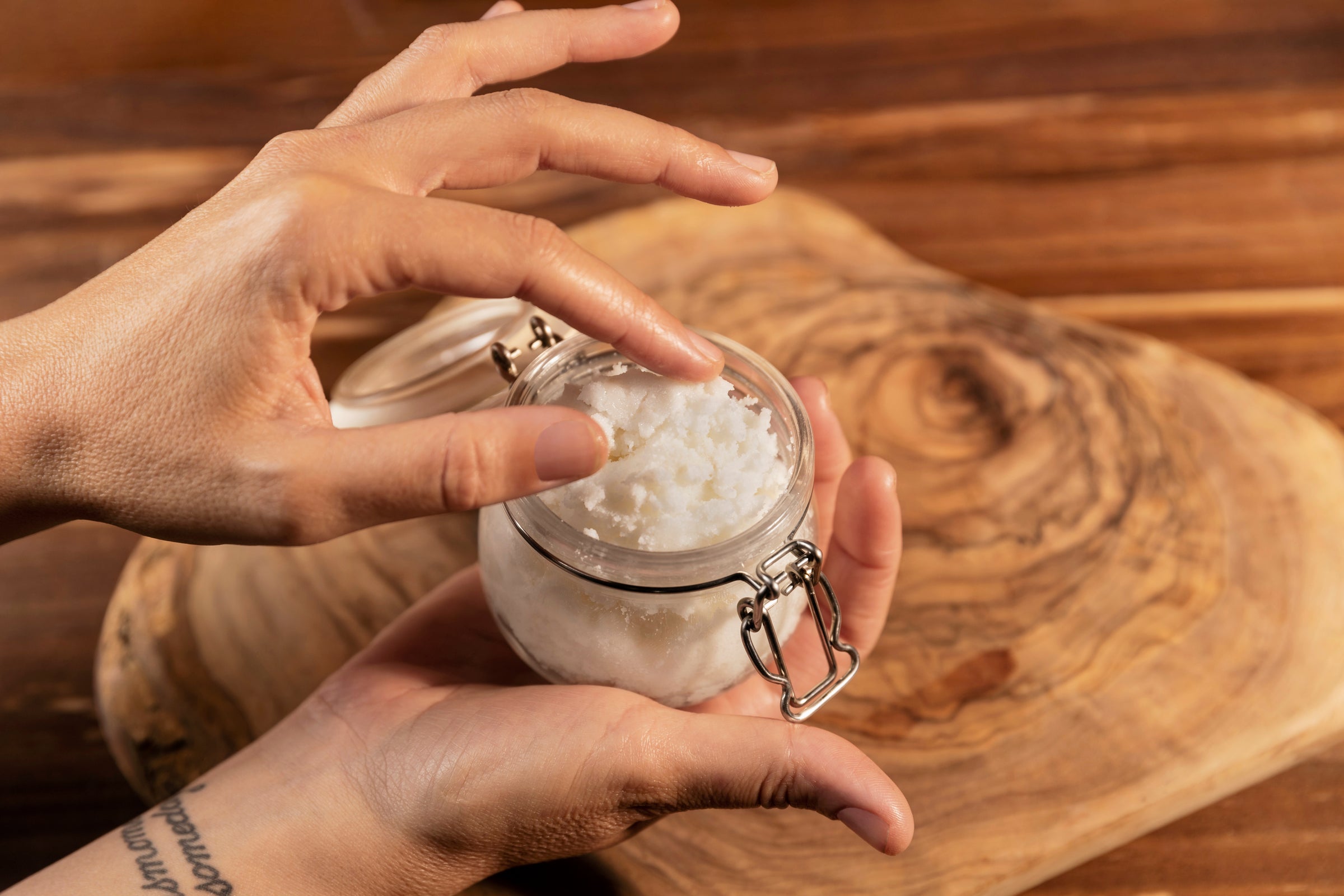 Sheep Tallow Creme im Glas in Händen vor rustikalem Holztisch