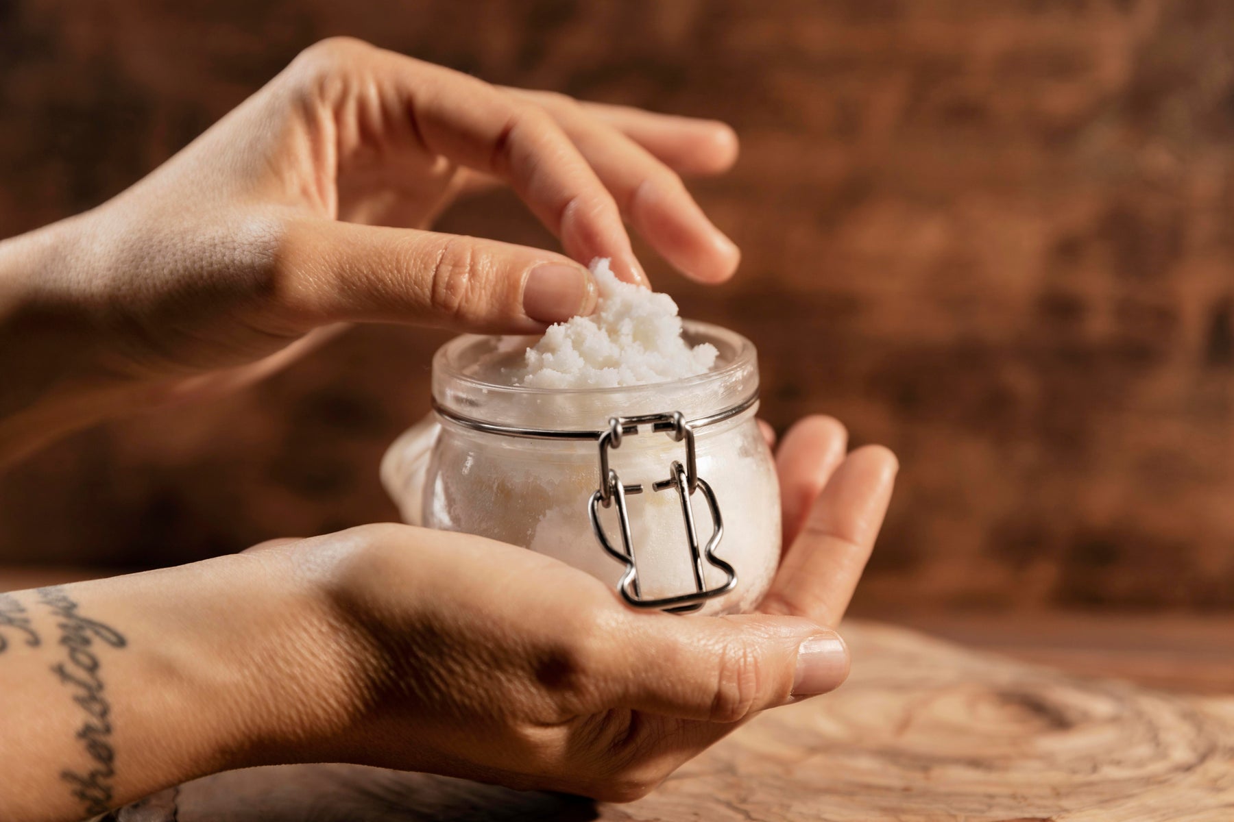 Sheep Tallow Creme im Glas in Händen vor rustikalem Holztisch